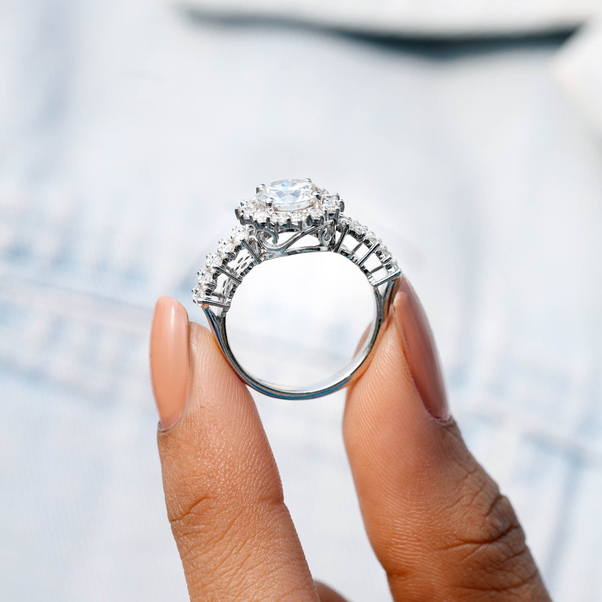 Silver ring with a large diamond held by a hand against a blurred background